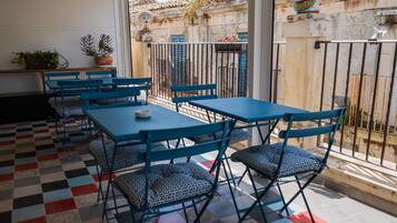 Een terras met blauwe tafels en stoelen, een geruit vloertje en plantenbakken.
