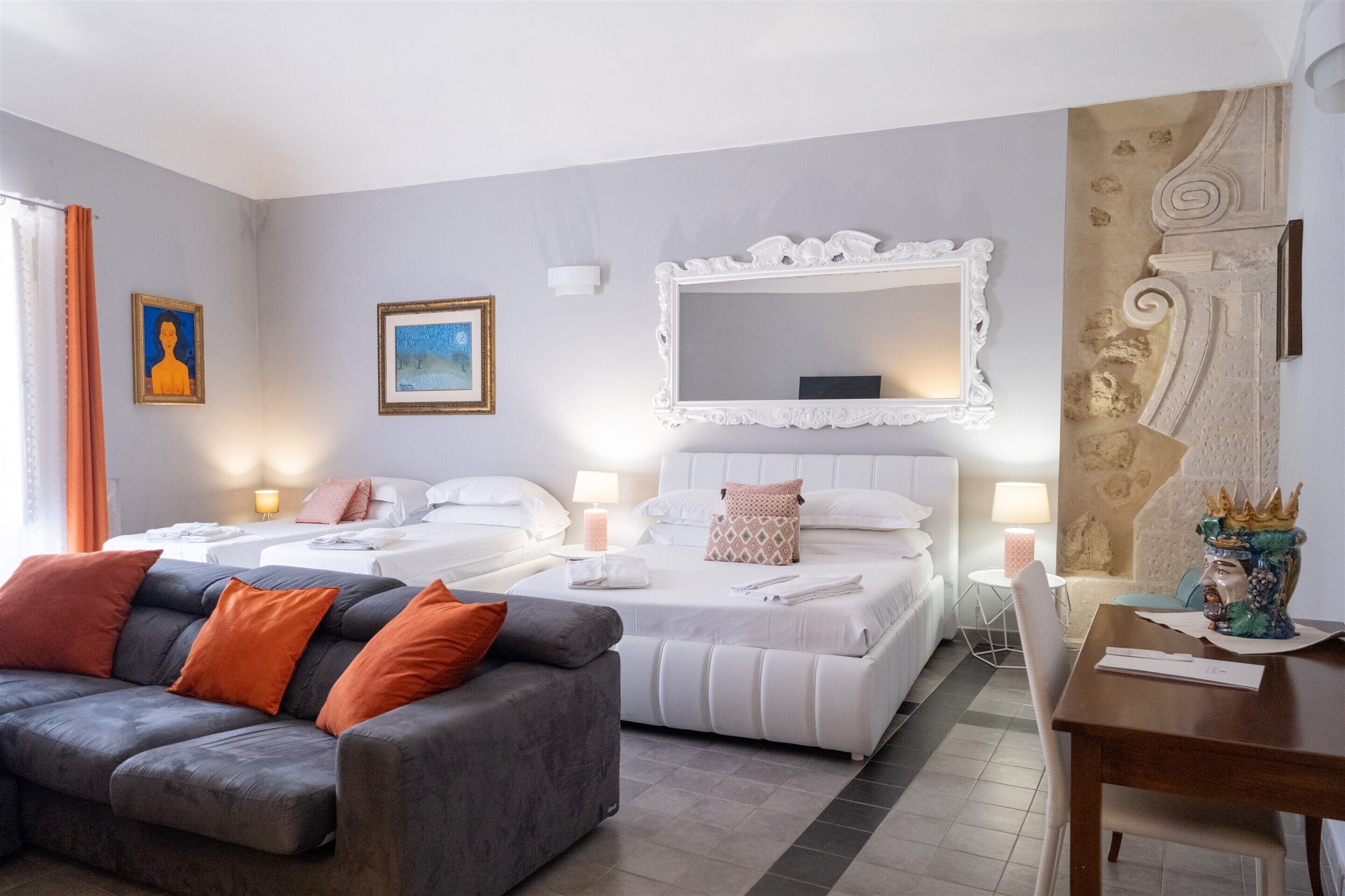 A hotel room with two beds, a sofa, a dining table, and decorative items.
