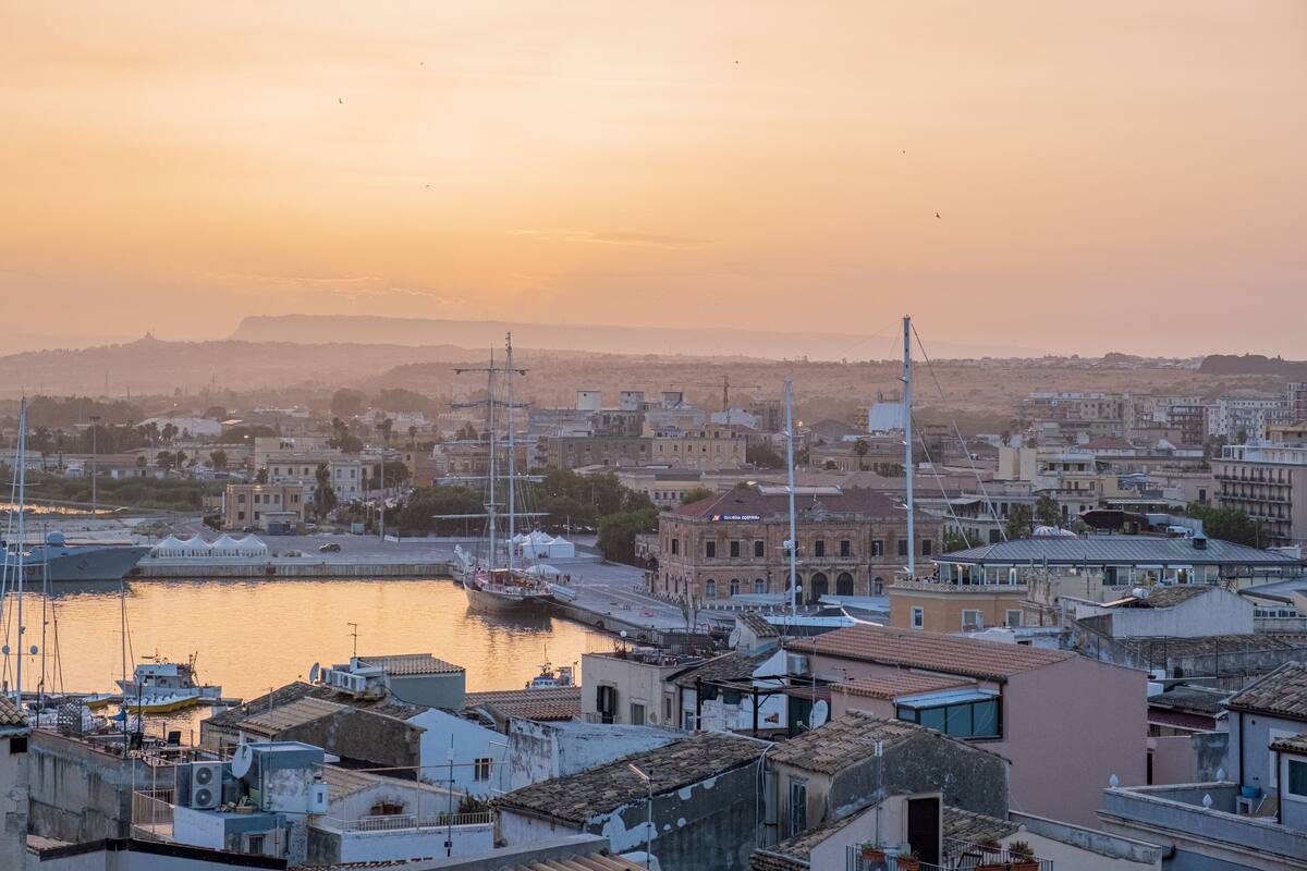 A coastal cityscape with a marina, buildings, and a sunset.