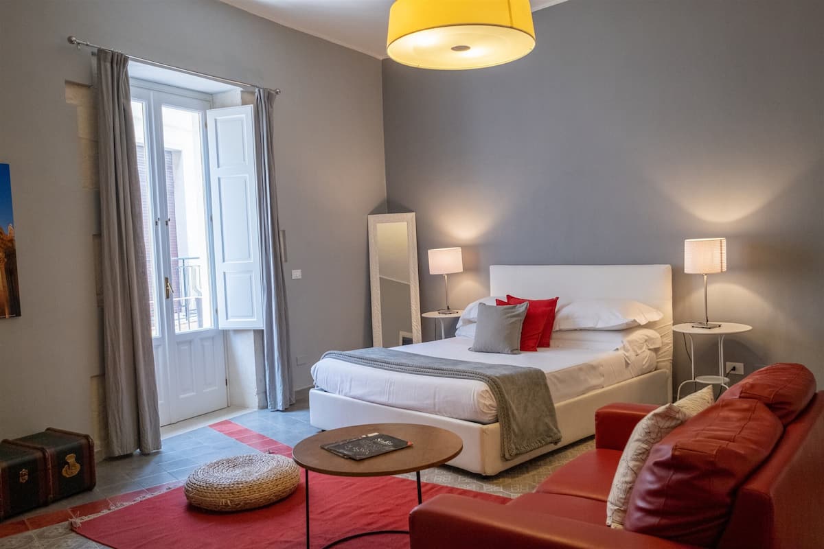 A modern bedroom with a large bed, bedside lamps, a red sofa, and a small round table.