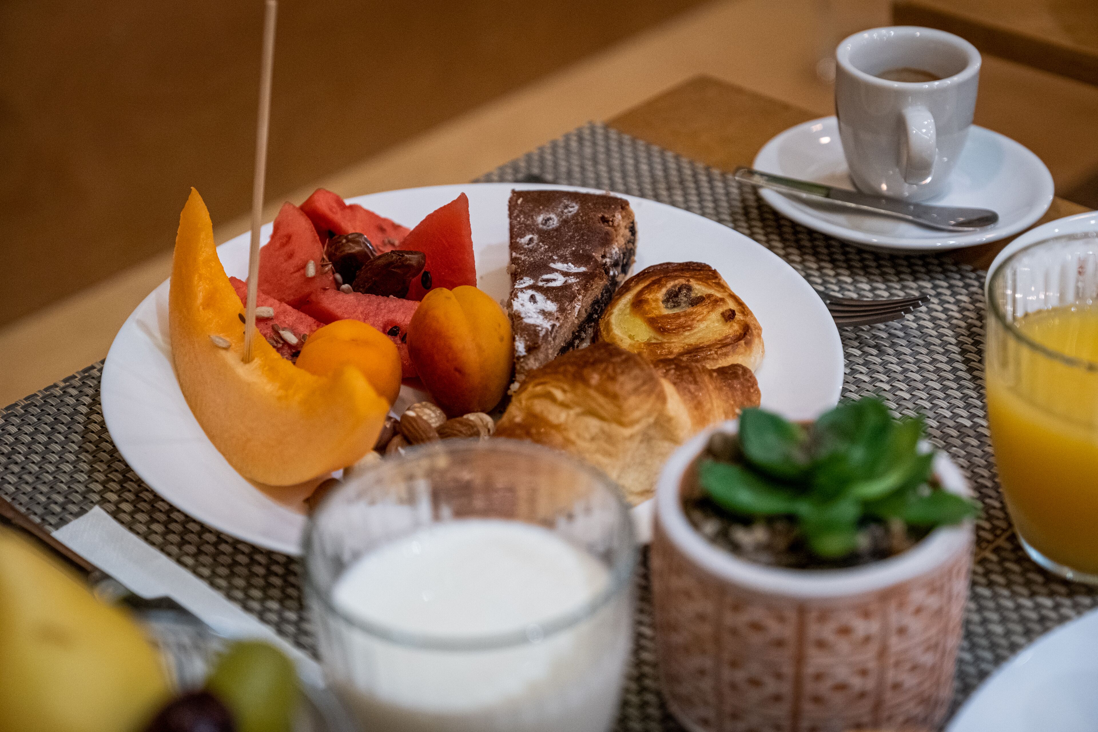A breakfast plate with various foods, a cup of coffee, a glass of orange juice, and a small potted plant.