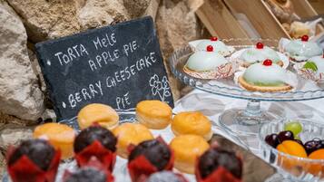 Una mesa con repostería variada y un cartel de tiza que enumera productos como Torta Mel, Pastel de Manzana y Cheesecake de Frutos Rojos.