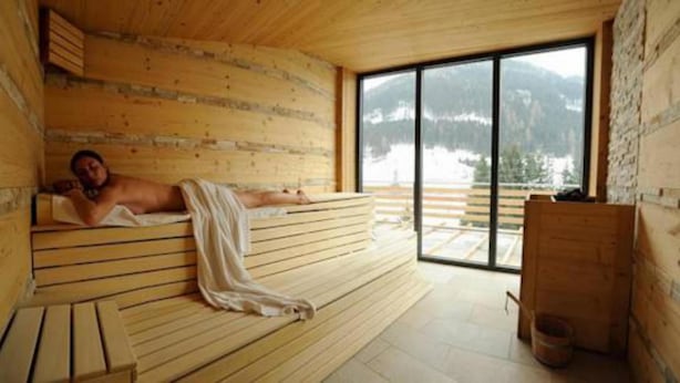 A wooden sauna with a bench, a large window, and a view of mountains. - Alpenlife Hotel Someda (Moena)