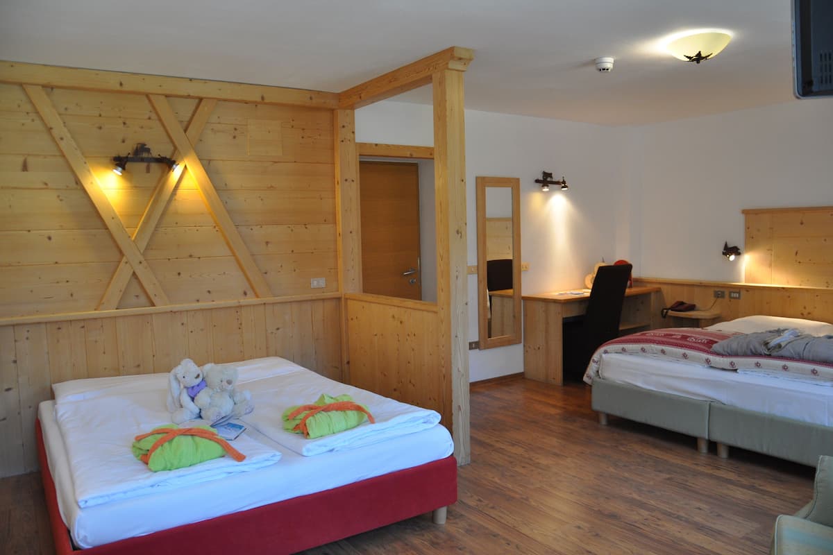 Een kamer met een houten plafond, een bed met een rode voetstuk, een bureau met stoel en een spiegel aan de muur.