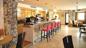 A bar area with a counter, red bar stools, and a seating area with tables and chairs. - Alpenlife Hotel Someda (Moena)