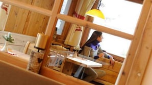 A wooden interior with a table and chairs, a window with a view, and a hanging lamp. - Alpenlife Hotel Someda (Moena)