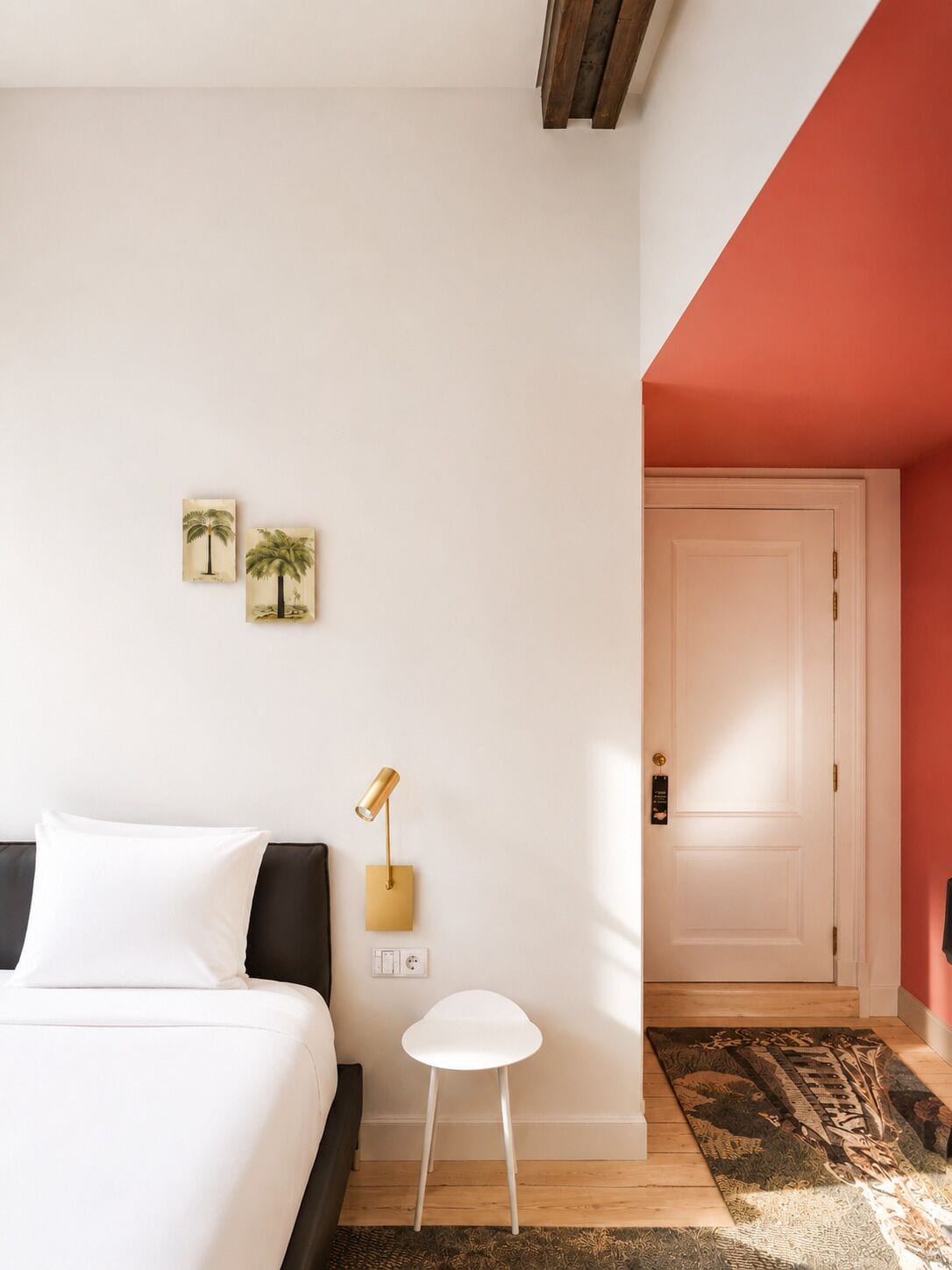 Een slaapkamer met een bed, een klein wit tafeltje, een lamp en twee decoratieve wandobjecten.