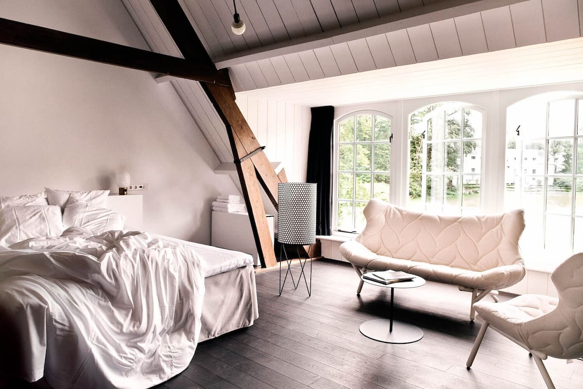 Ein Schlafzimmer mit einem Bett, einem Sessel, einer Lampe und großen Fenstern.