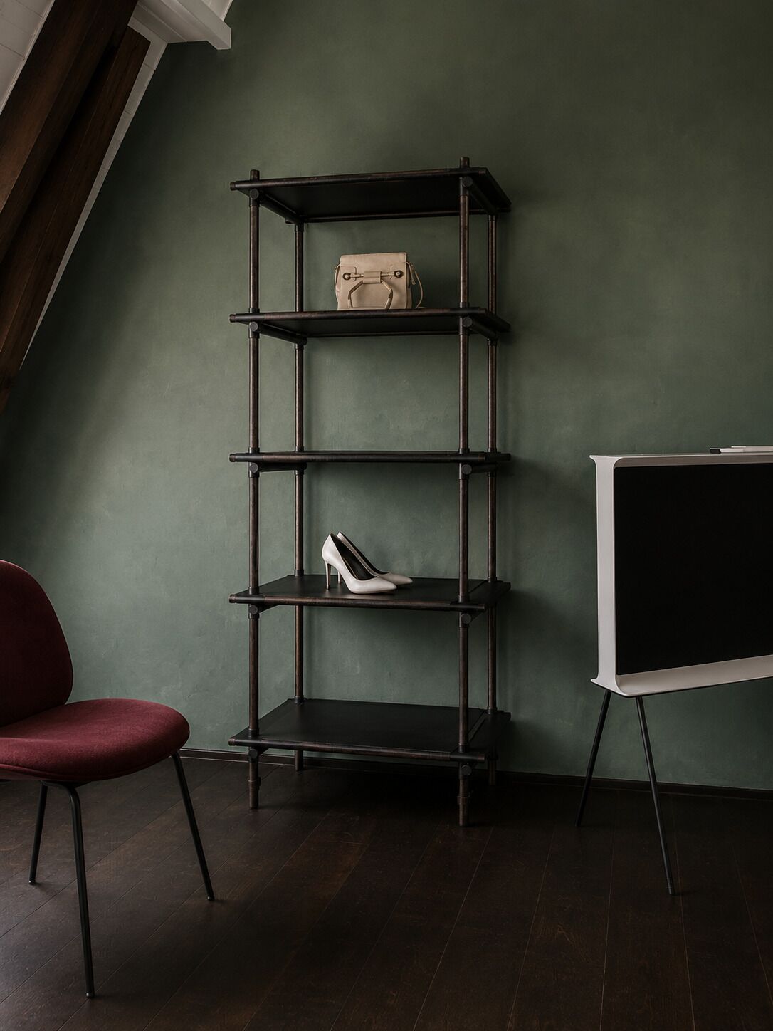 A room with a dark wooden floor, a red chair, a black and white shelf unit, and a whiteboard.