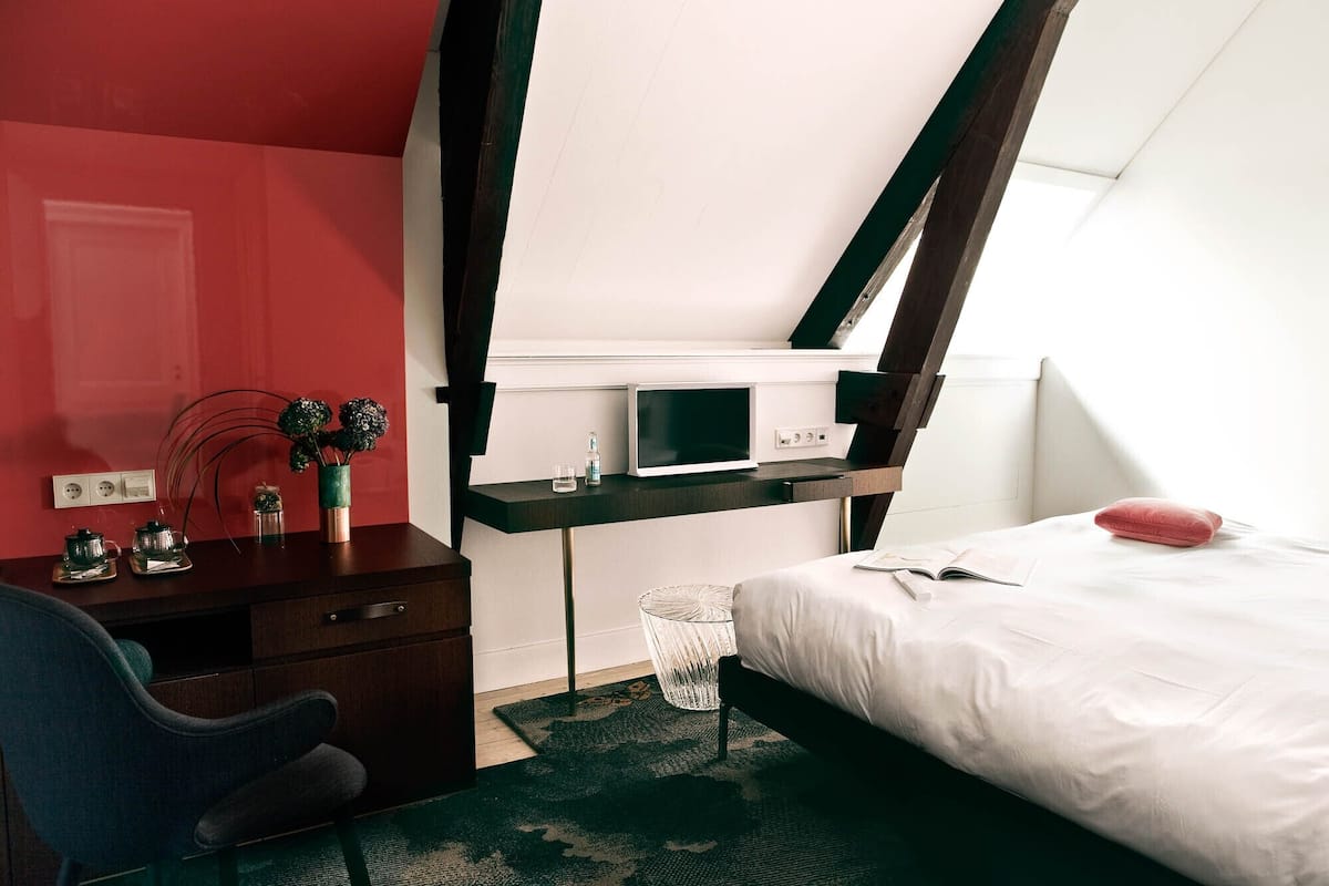 Ein modernes Schlafzimmer mit einem Bett, einem Schreibtisch mit Computer, einem Sessel und einem kleinen Tisch mit Dekoration.