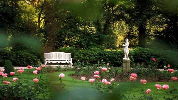 Un jardín con una estatua, un banco blanco y flores rosadas.