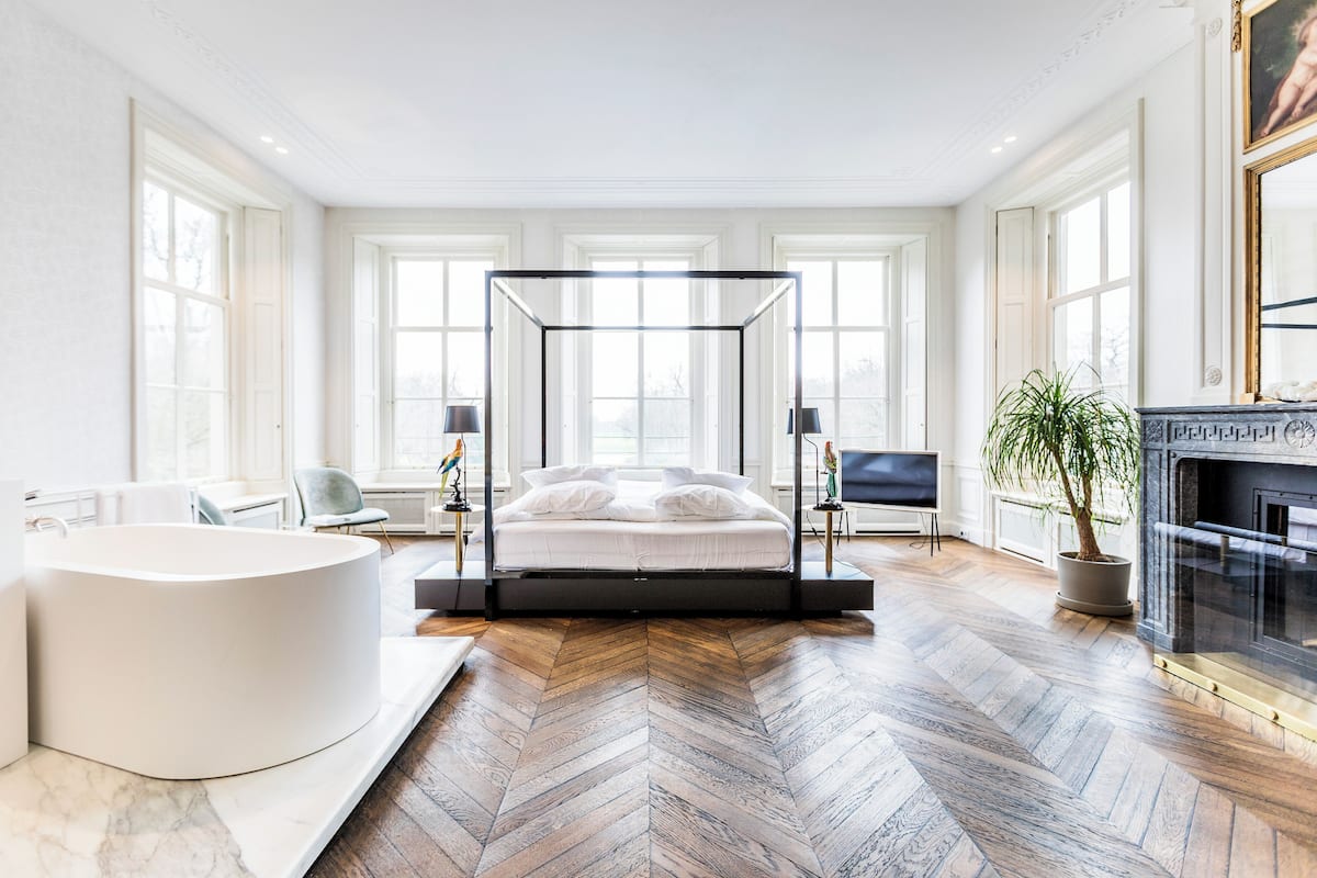 Ein modernes Schlafzimmer mit einem Himmelbett, einer großzügigen Badewanne und einem Kamin.