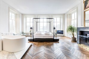 Une chambre à coucher moderne avec un lit à baldaquin, une grande baignoire et une cheminée.