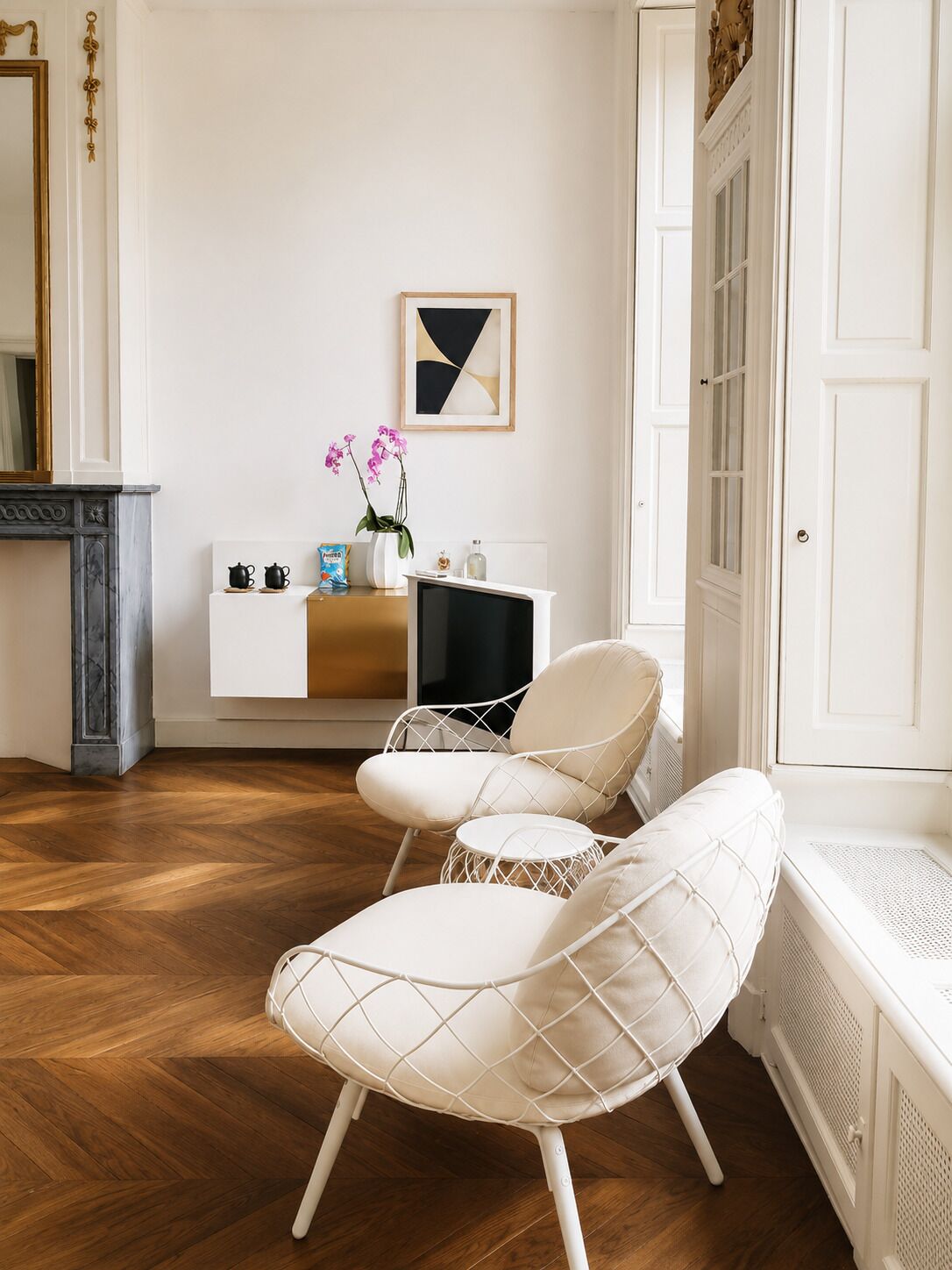 Une pièce avec un plancher en bois, des meubles blancs, une cheminée et un tableau encadré au mur.