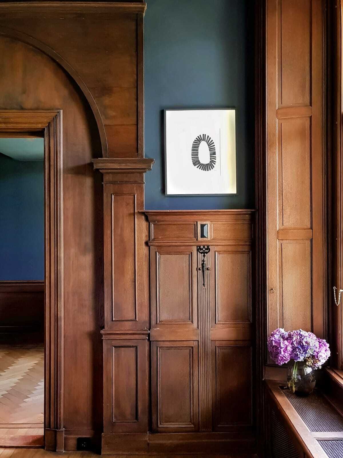 A room with a wooden cabinet, a framed artwork, and a vase with flowers.