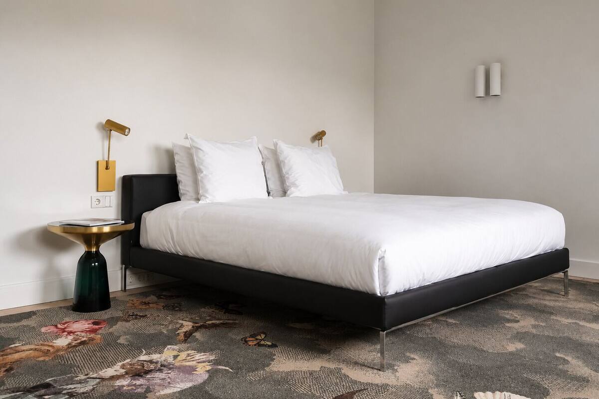 Ein Schlafzimmer mit Bett, Nachttisch, Lampe und Wandleuchte.