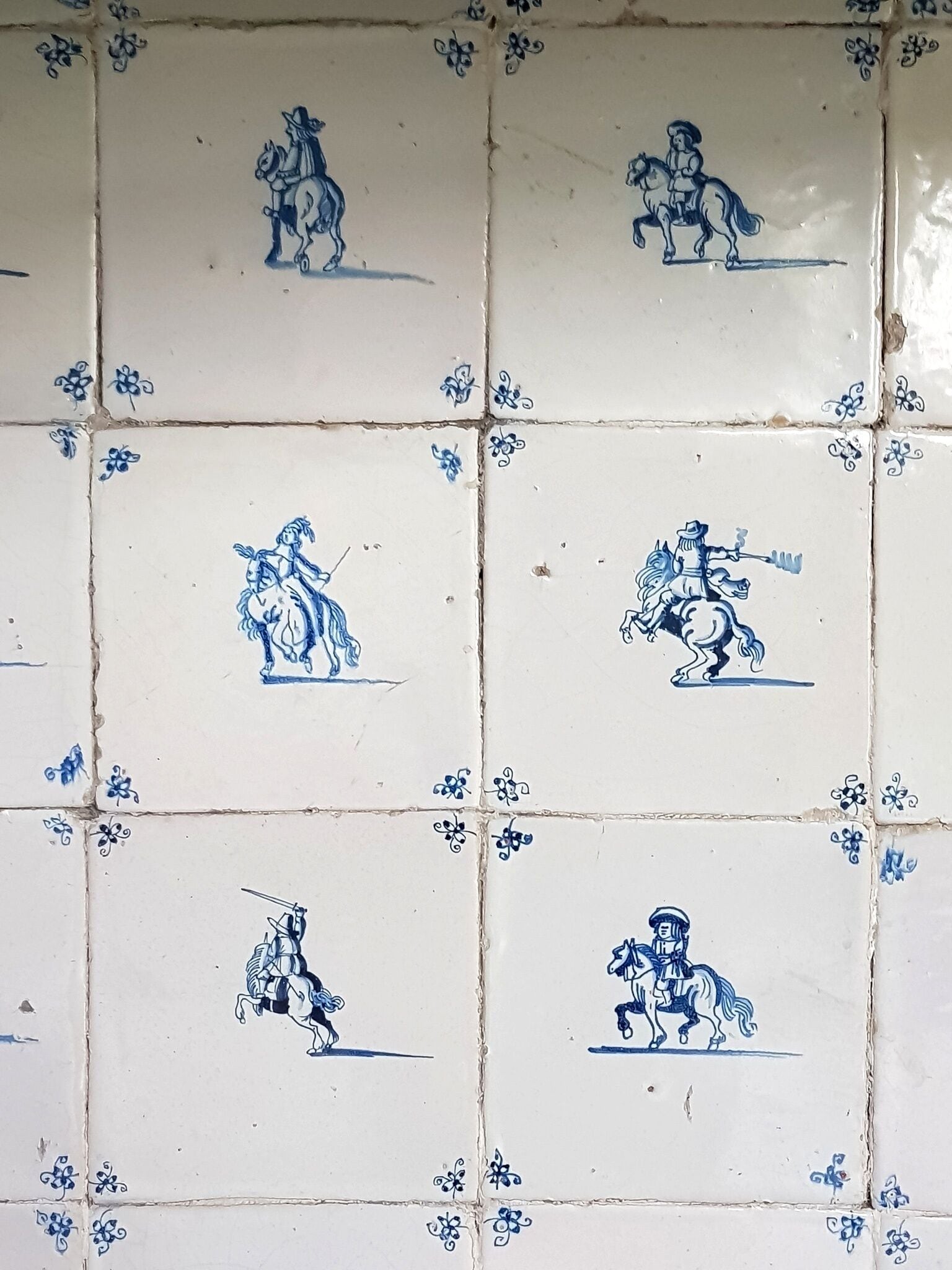 Un muro piastrellato con motivi blu e bianchi, tra cui figure a cavallo.