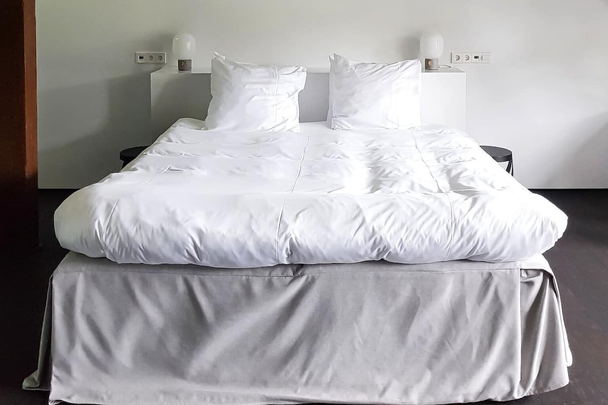 Ein Schlafzimmer mit einem Bett, weißer Bettwäsche, einer Holzbalkendecke und einer Lampe.