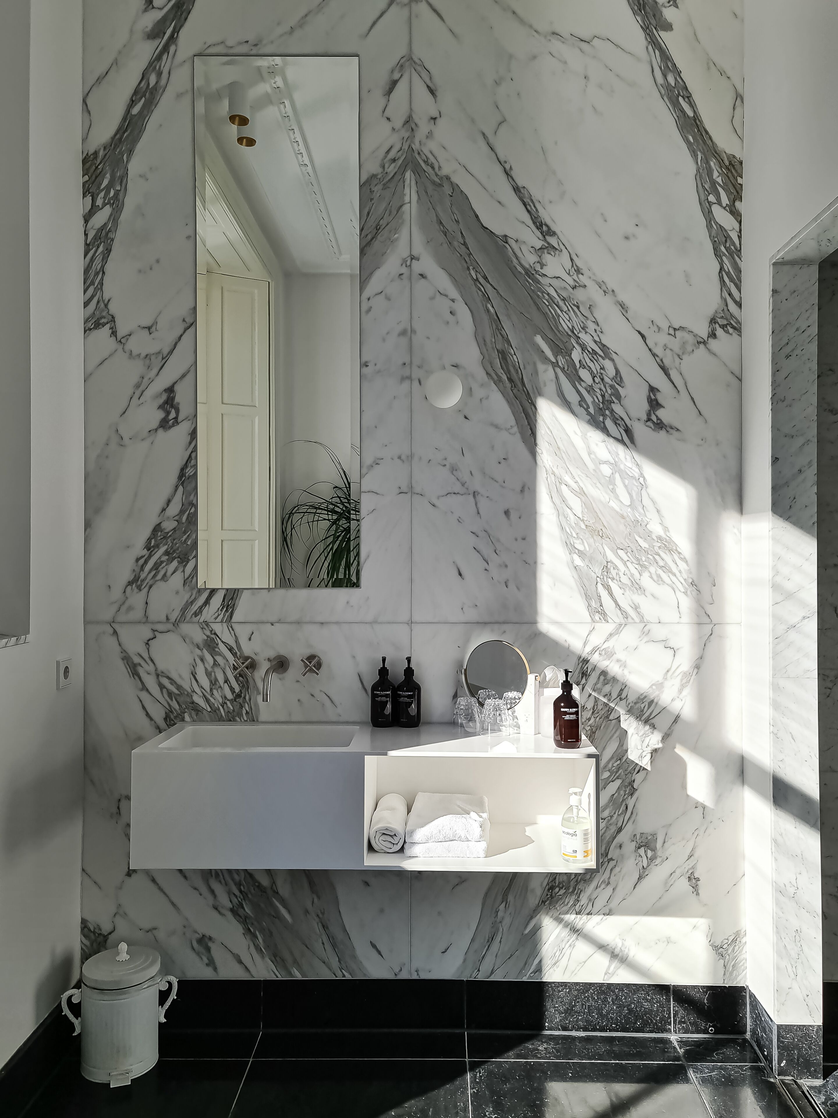 Une salle de bain avec un pare-baignoire en marbre, un lavabo avec un miroir au-dessus et un porte-serviettes avec des serviettes.