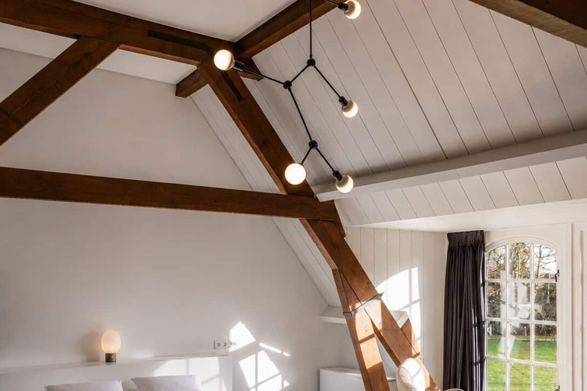 Ein Schlafzimmer mit einem großen Bett, einem Sessel, einem Fenster und einer Decke mit freiliegenden Balken.