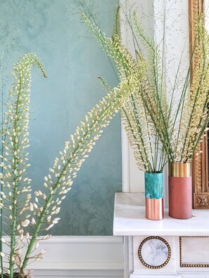 Une console blanche sur laquelle sont posés deux vases contenant de grandes plantes vertes.