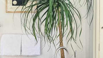 Une salle de bain avec une baignoire, une plante en pot, un tableau encadré et un porte-serviettes.