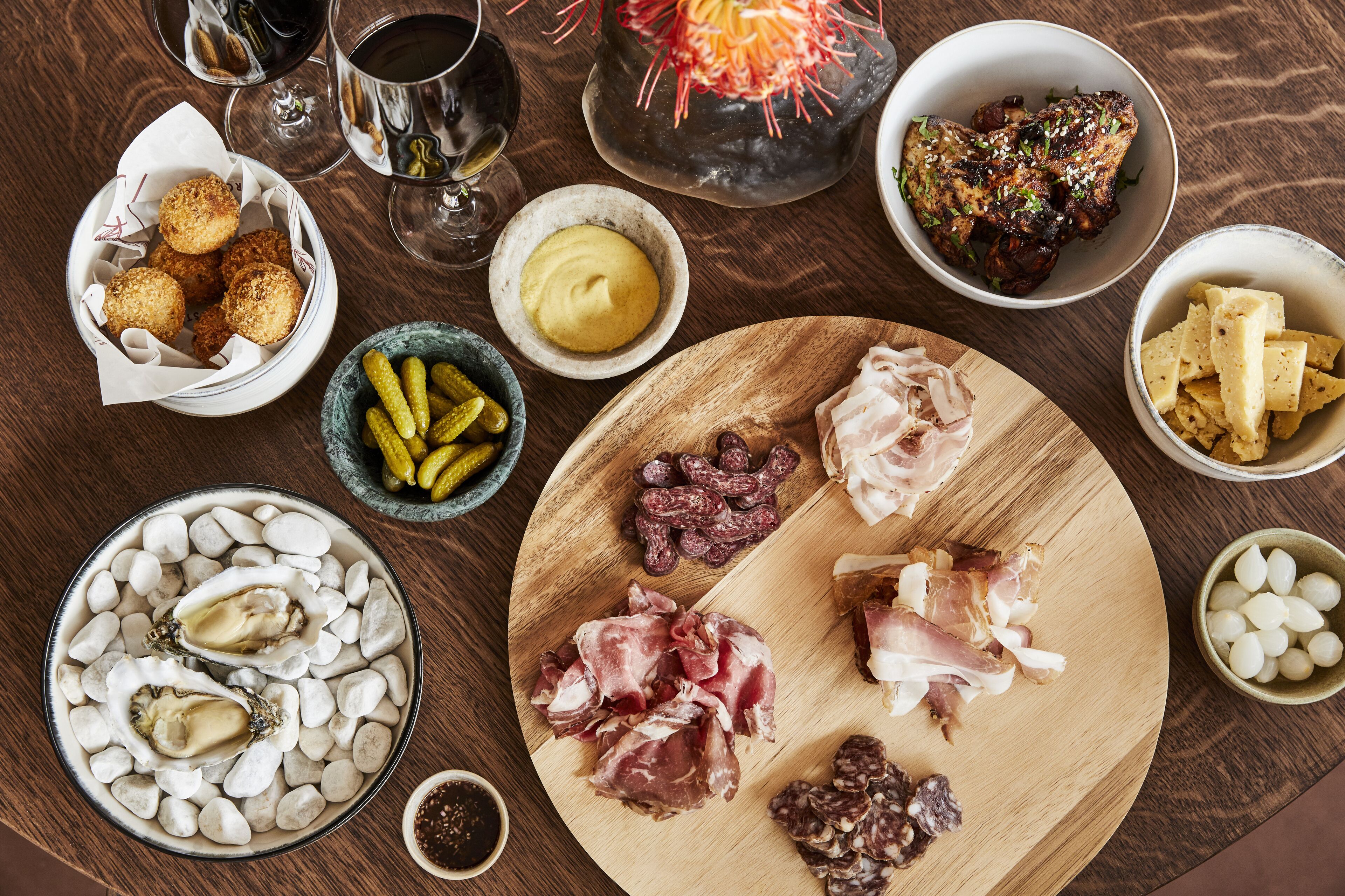 A wooden table with various food items, including oysters, meats, and cheeses, arranged for a meal.