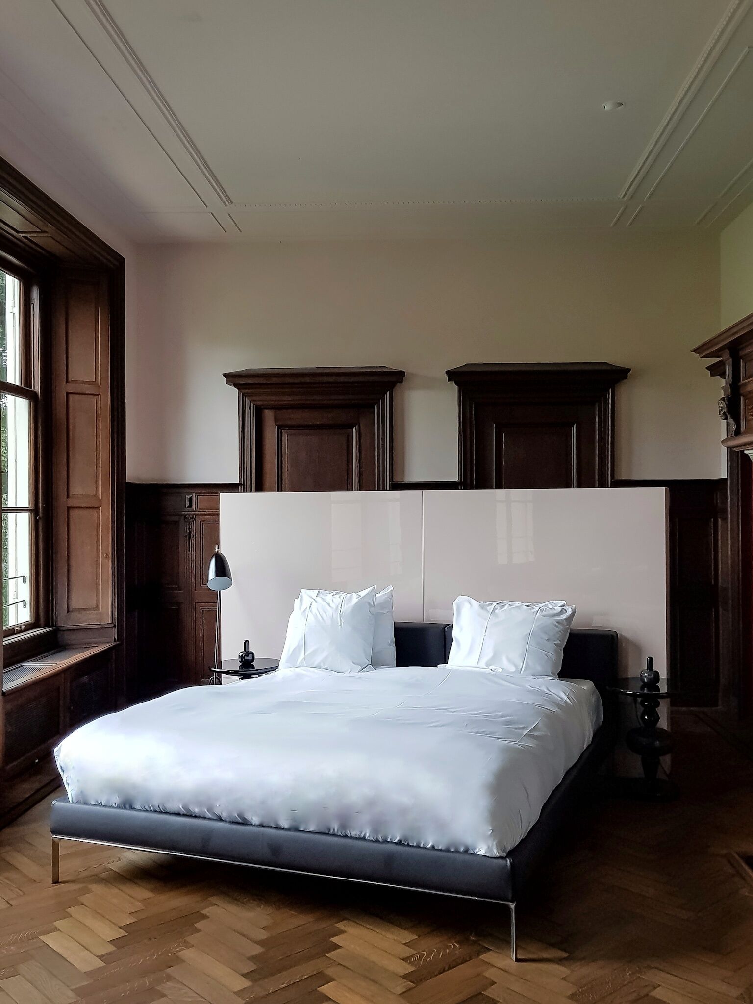 Una cama grande con estructura metálica, ropa de cama blanca y dos cabeceros de madera oscura.