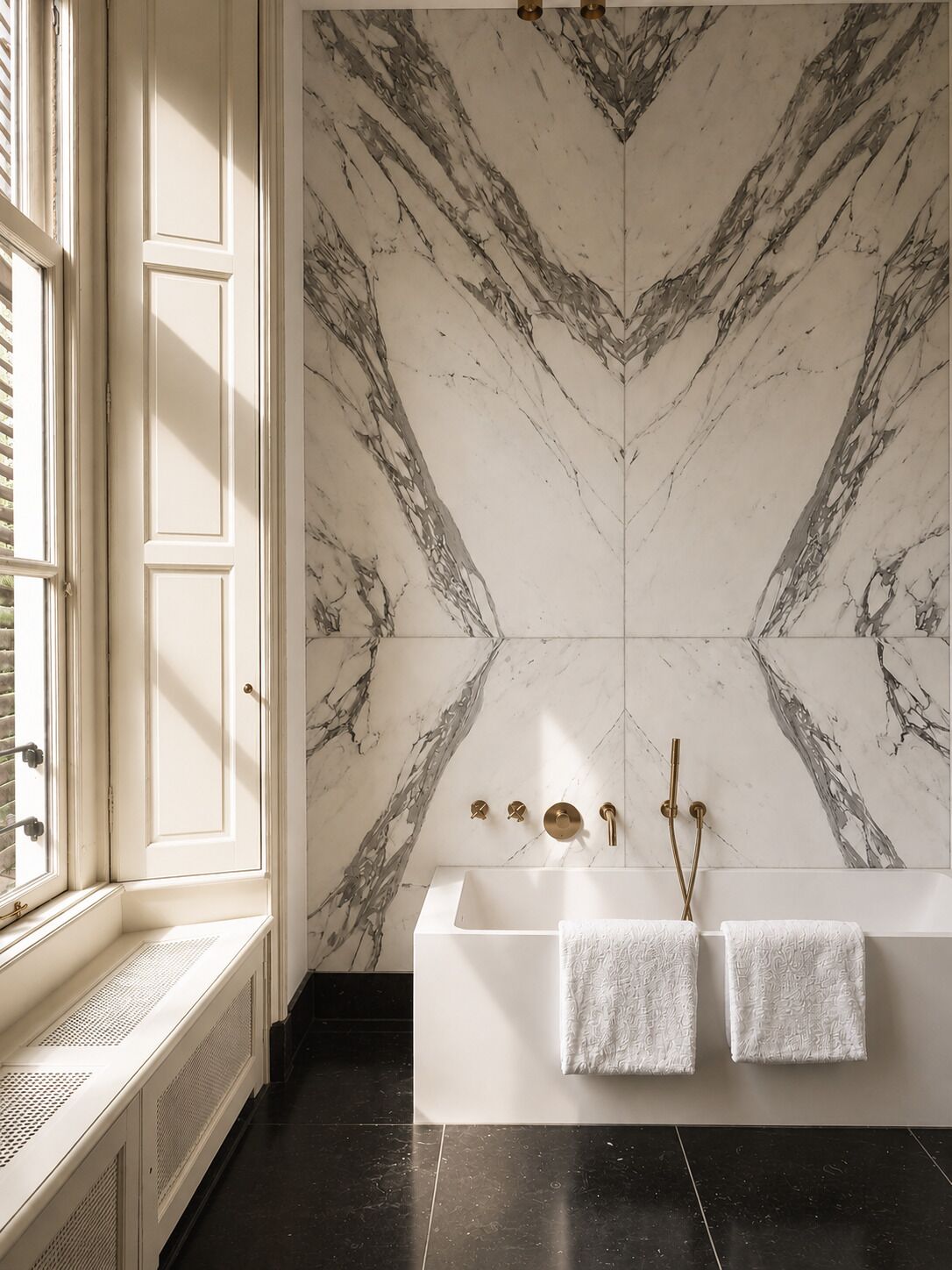 A bathroom with a marble wall, a bathtub, and two towels.