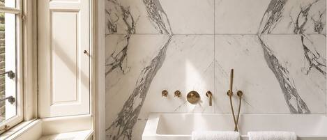 A bathroom with a marble wall, a bathtub, and two towels.