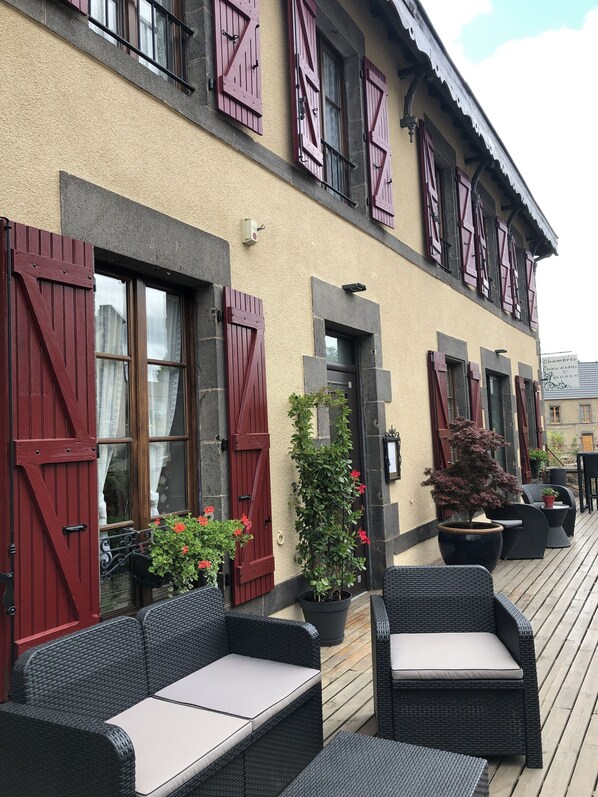 A building with red shutters, outdoor wicker furniture, and potted plants. - A l'Aube des Volcans (Charbonnières-les-Vieilles)