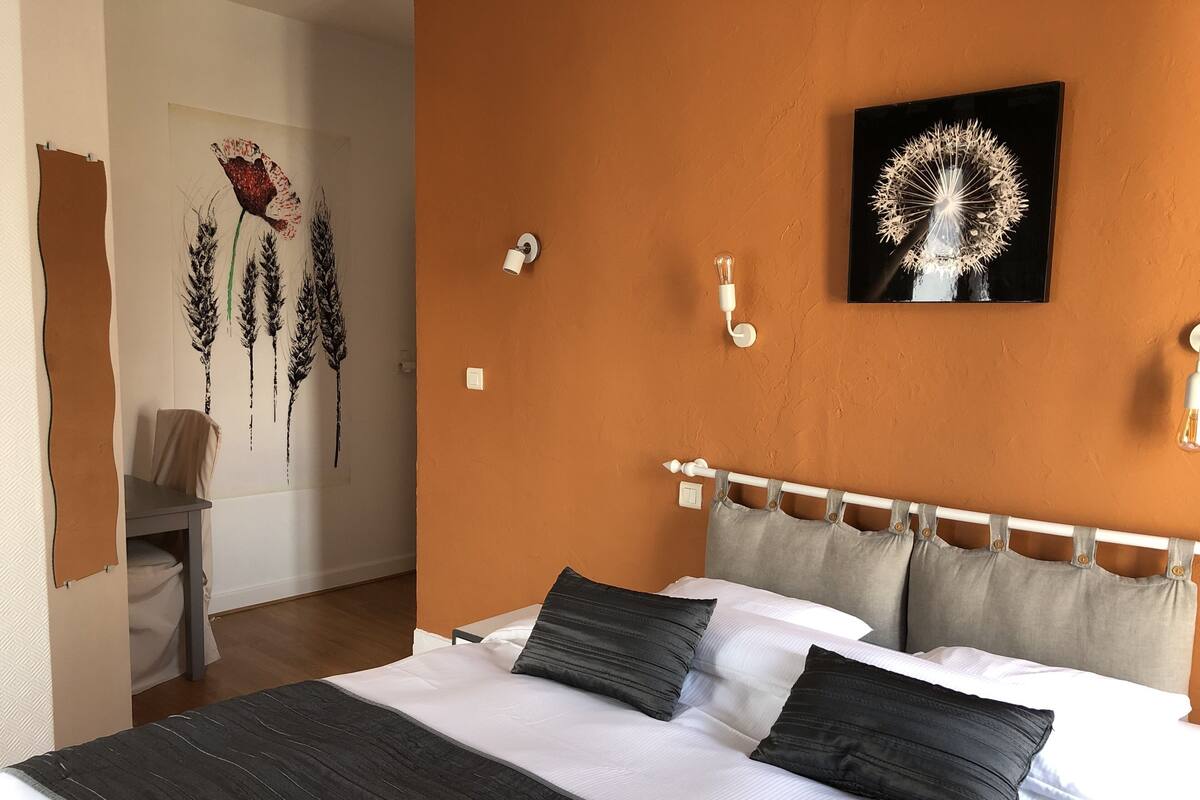 A bedroom with a large bed, white and grey bedding, a white headboard, and a wall-mounted light fixture.