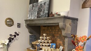 A wooden display cabinet with various items, a vase with flowers, and a fireplace with a brick surround. - A l'Aube des Volcans (Charbonnières-les-Vieilles)