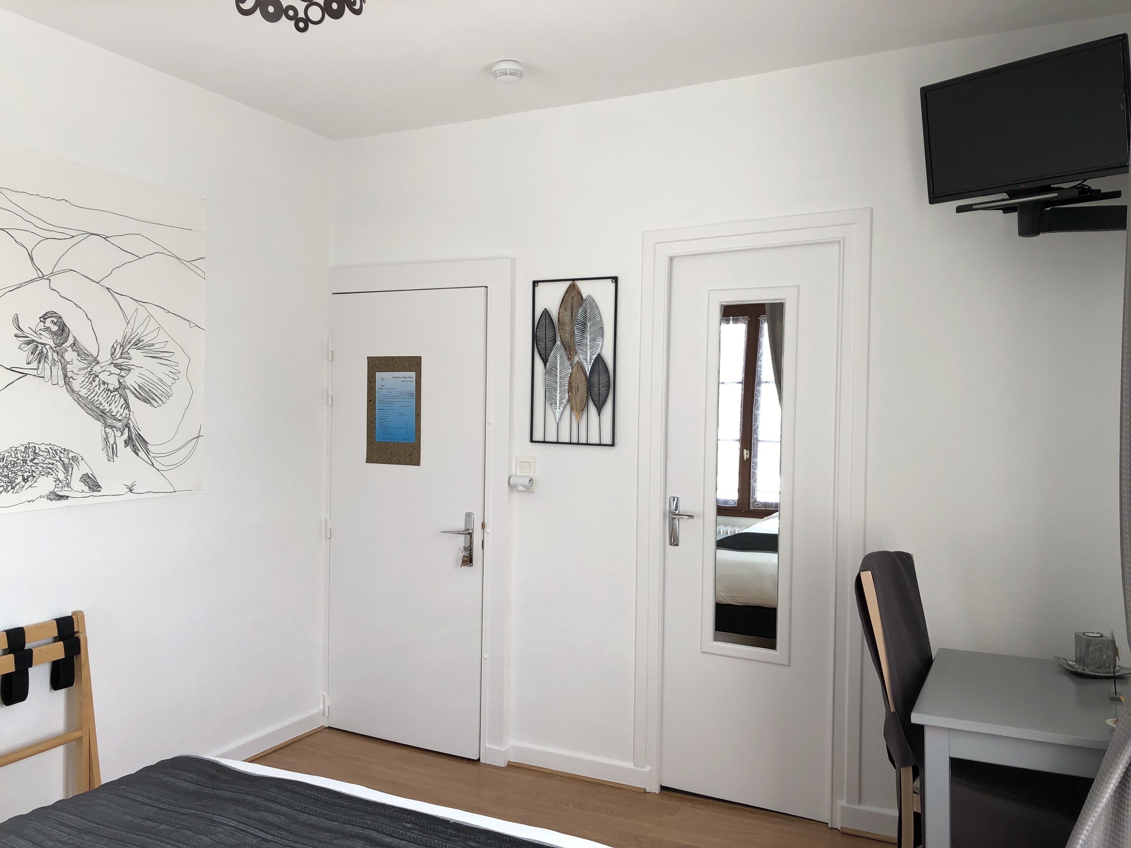 Une chambre à coucher avec un lit, un bureau, une chaise, une télévision et une porte dotée d’un miroir.