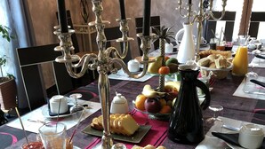 A breakfast table with various food items, a pitcher of orange juice, and a candelabra with candles. - A l'Aube des Volcans (Charbonnières-les-Vieilles)