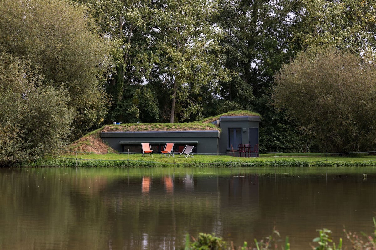 A lakeside building with a small dock, a covered seating area, and a grassy hill.
