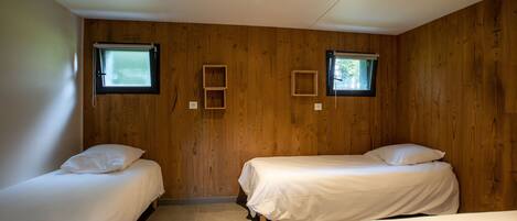 A room with two beds, wooden walls, and two windows.