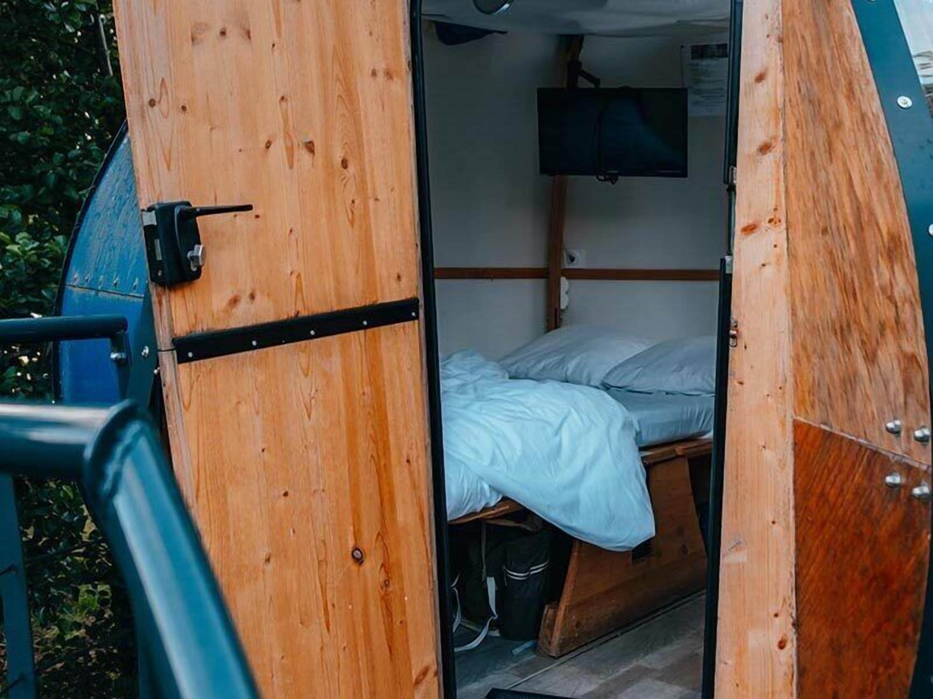 Ein kleiner, abgeschlossener Raum mit einem Bett, einem an der Wand befestigten Fernseher und einer Tür mit Griff.