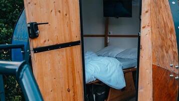 Ein kleiner, abgeschlossener Raum mit einem Bett, einem an der Wand befestigten Fernseher und einer Tür mit Griff.