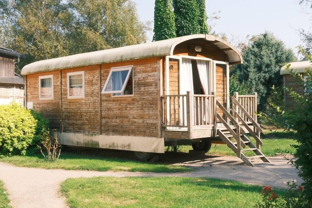 A wooden RV with a covered porch, windows, and a staircase leading to the entrance.