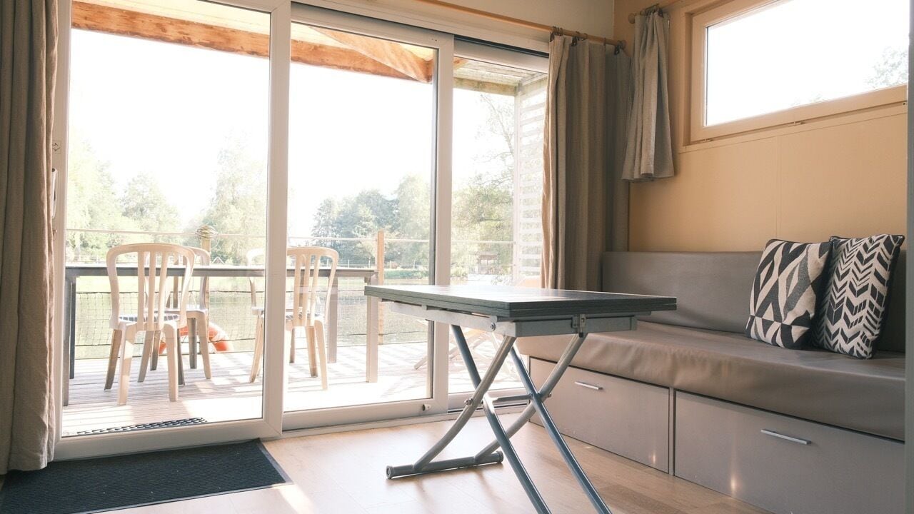 Une pièce dotée d’une porte-fenêtre coulissante donnant sur un balcon, d’un canapé agrémenté de coussins à motifs et d’une petite table.
