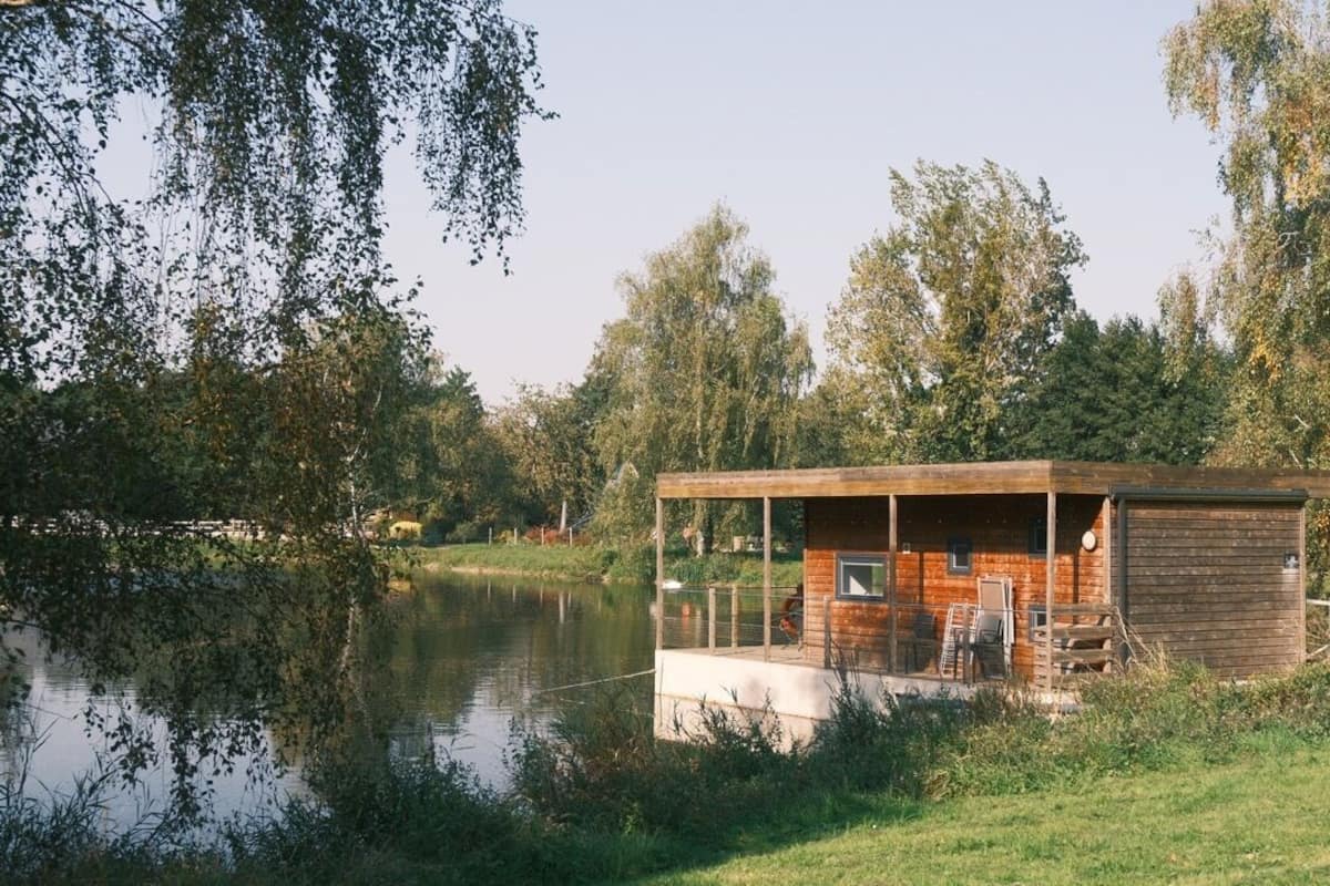 A wooden cabin by a lake with a dock, surrounded by trees.