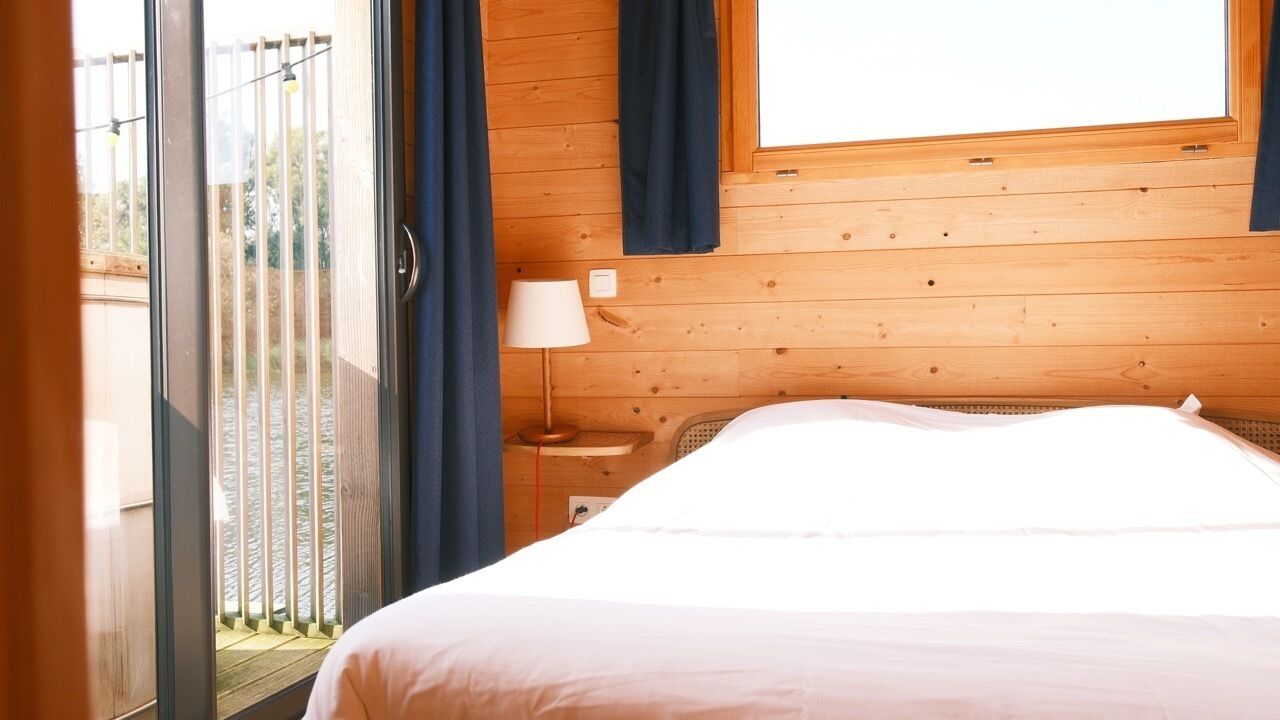Una habitación con cama, ventana con cortinas, lámpara y vista a un balcón.