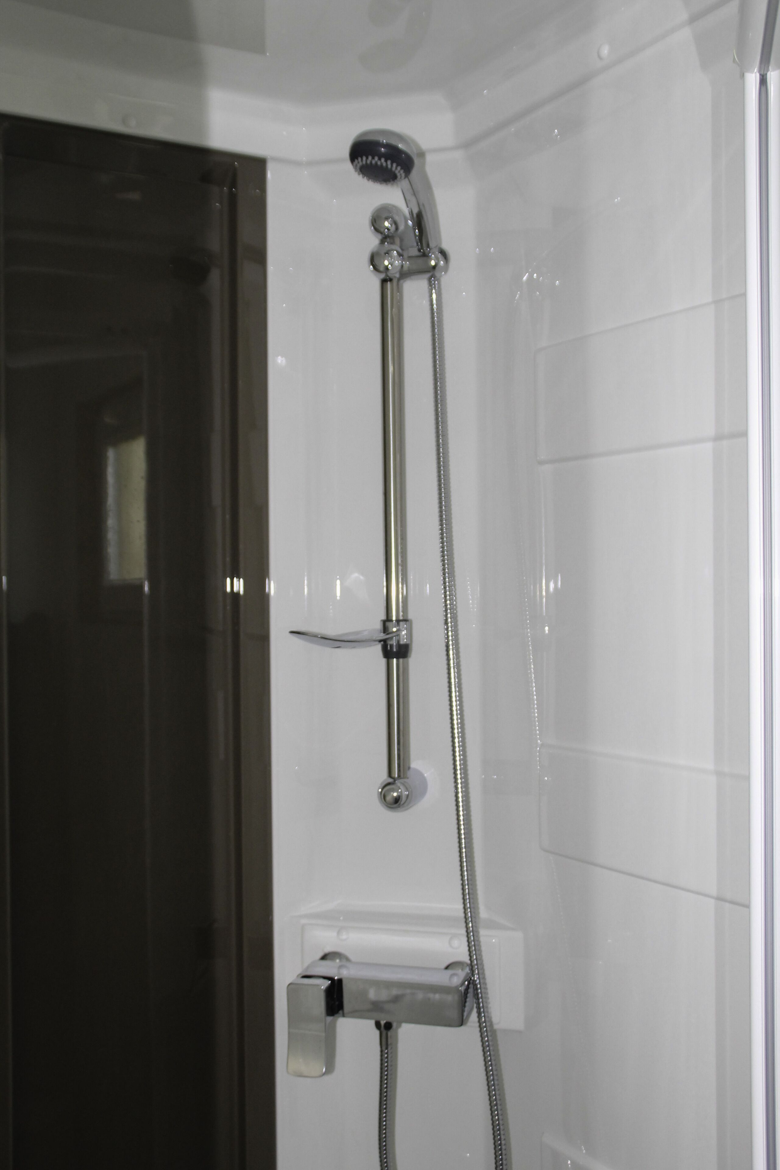 A shower with a handheld showerhead and a wall-mounted faucet.