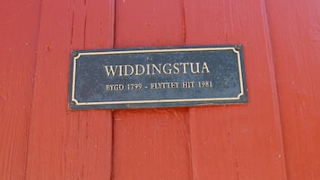A plaque on a red wooden surface with the text "WIDDINGSTUA BYGD 1799 - FLYTTET HIT 1981".