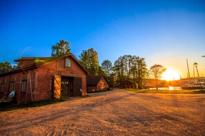 A brick building with a garage door, a dirt road, and trees in the background.