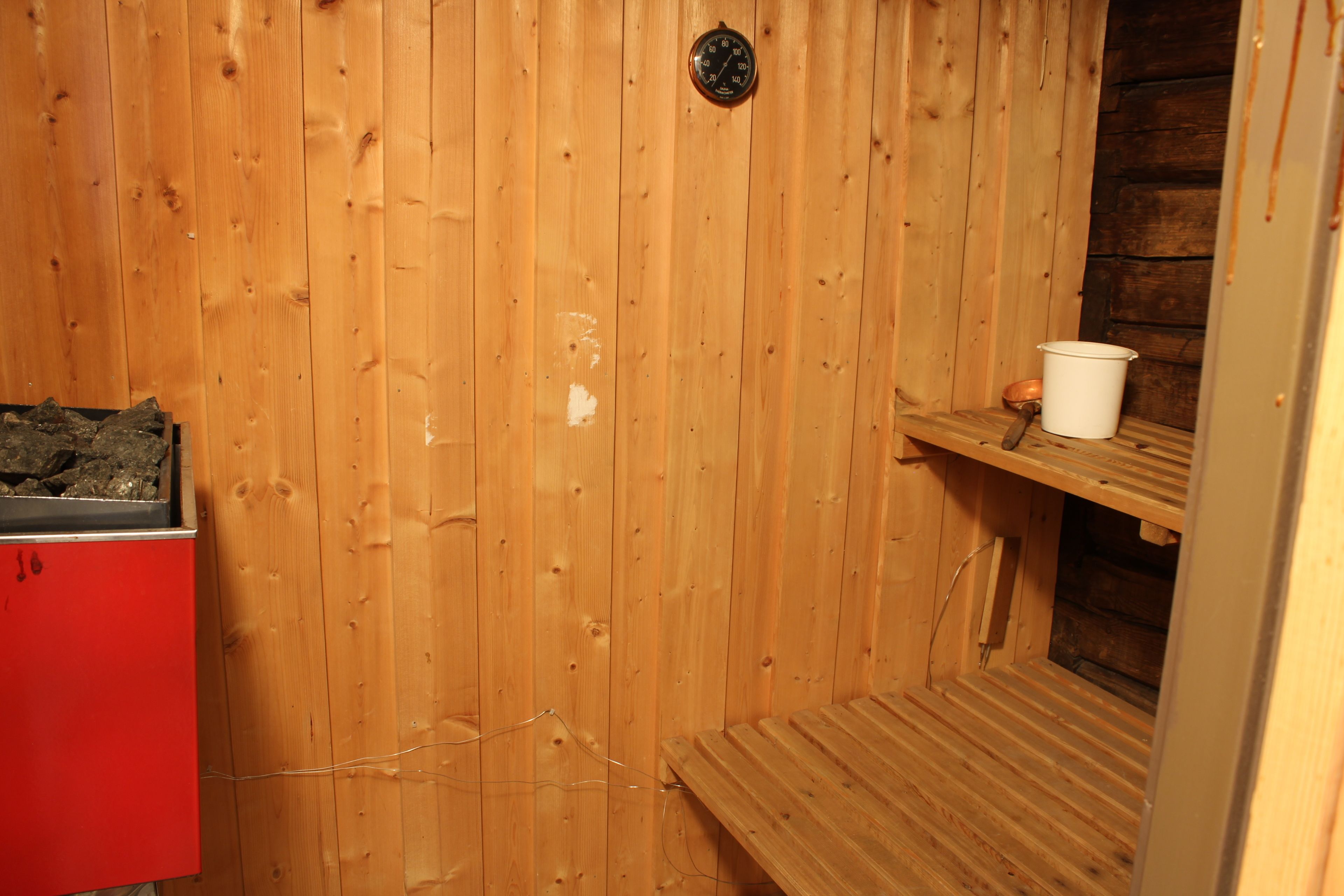 Una sala de sauna con paredes de madera, un banco, un balde blanco y un armario rojo.