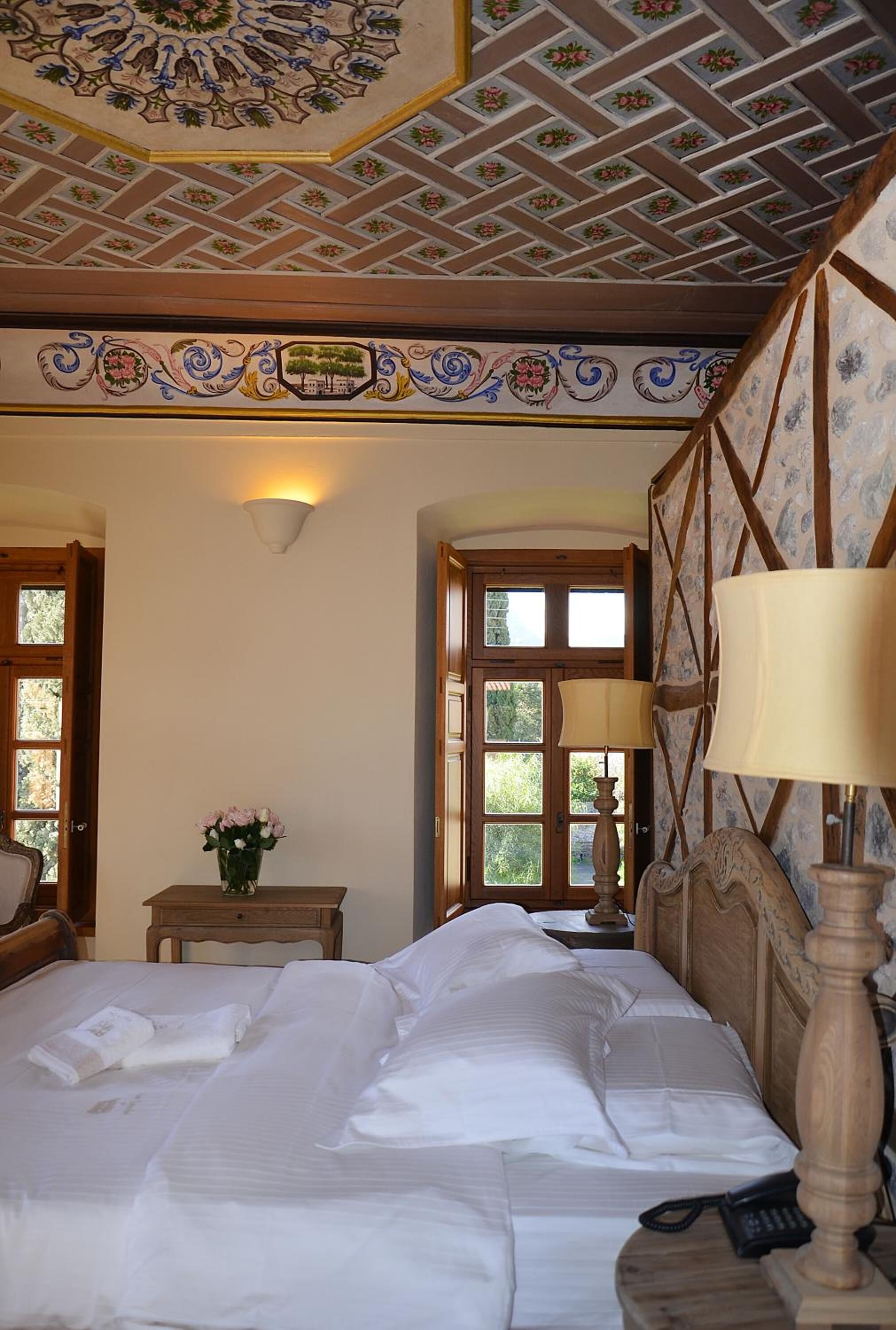 A bedroom with a bed, a nightstand, a lamp, a wall-mounted light, and a decorative ceiling.