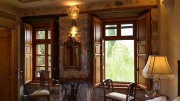 A room with a stone wall, wooden furniture, a mirror, and large windows.