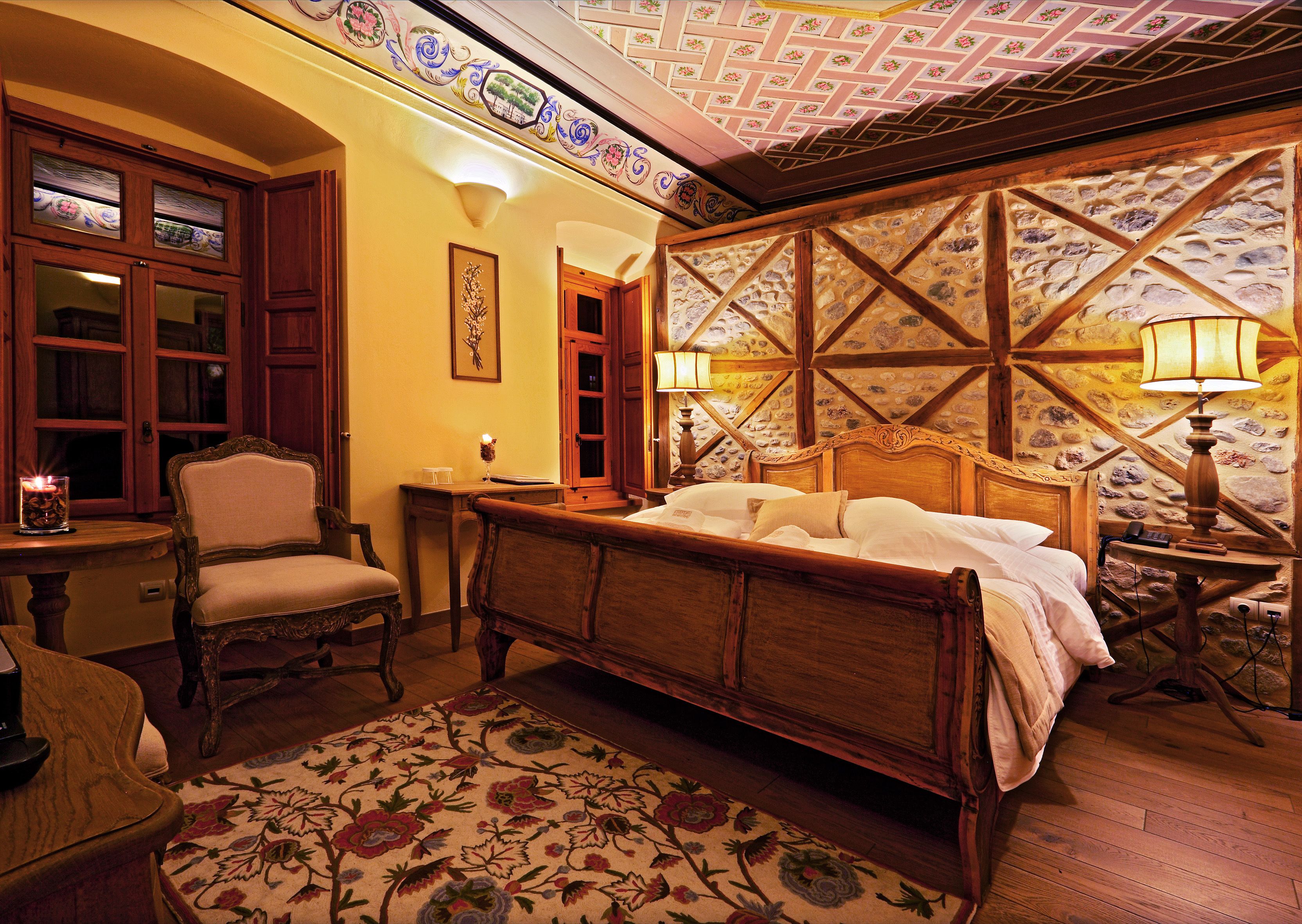 Een traditionele slaapkamer met een houten bed, een stoel, een tafel met een lamp en een kamerkleed met dessin.
